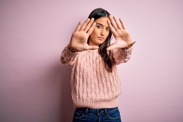 Young beautiful brunette woman wearing casual sweater over isolated pink background doing frame using hands palms and fingers, camera perspective