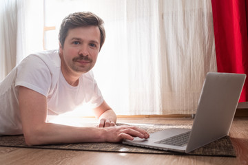 Handsome strong sportsman on floor in living room using laptop computer for online web lesson.