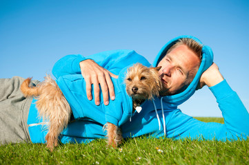 Dog and best friend owner in matching blue hooded sweatshirts bonding outdoors on sunny green field
