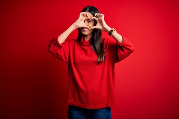 Young beautiful brunette woman wearing casual sweater over isolated red background Doing heart shape with hand and fingers smiling looking through sign