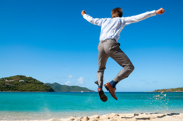 Excited businessman celebrating on a tropical beach jumping into the air clicking his heels together