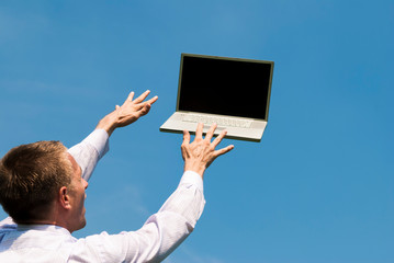 Businessman reaching out to type on laptop computer floating away in blue sky