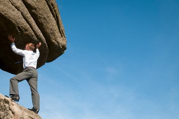 Strong businessman lifting massive rock boulder into blue sky copy space