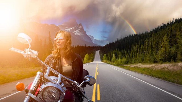 Cinemagraph Continuous Loop Animation. Caucasian Biker Woman on a Motorcycle on a scenic Road in the Canadian Rockies. Image Composite. Background from Banff, Alberta, Canada.