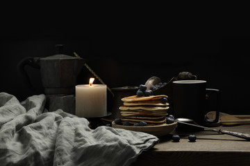 national dish pancakes, pancakes, pita with blueberries, linen napkin, a candle burns, a cup of tea, an old mocha coffee machine, a concept of traditional cuisine