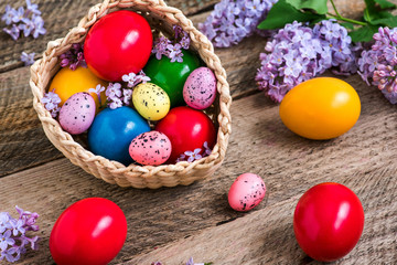 Fototapeta na wymiar Natural dye colored easter eggs in a basket and lilac flowers on rustic wooden table