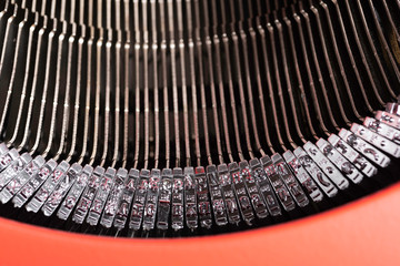 A close-up or a macro shot of the typebars of a retro-style manual typewriter encased in a hinged red top cover.