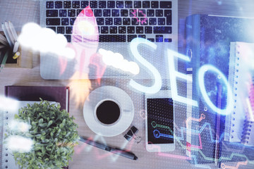 Double exposure of SEO hologram drawing over desktop. Top view. Search optimization concept.