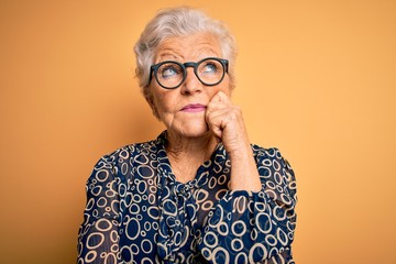 Senior beautiful grey-haired woman wearing casual shirt and glasses over yellow background with...