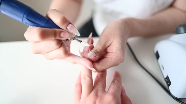 Hardware professional manicure process, cleaning of nails by a milling cutter. Close up female hands in beauty salon. Finger nail treatment, making process. Electric nail file drill in action