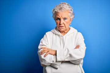 Senior beautiful sporty woman wearing white sweatshirt over isolated blue background skeptic and nervous, disapproving expression on face with crossed arms. Negative person.