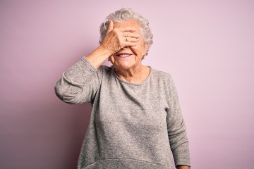 Senior beautiful woman wearing casual t-shirt standing over isolated pink background smiling and laughing with hand on face covering eyes for surprise. Blind concept.