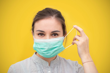 Young beautiful woman takes off protective sterile medical mask on a yellow background. Happy end. Victory over coronavirus. Pandemic Covid-19.