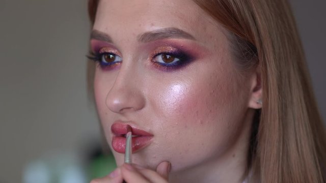 Makeup artist paints lips of a model girl.