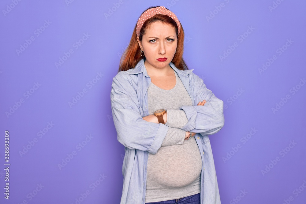 Poster Young beautiful redhead pregnant woman expecting baby over isolated purple background skeptic and nervous, disapproving expression on face with crossed arms. Negative person.