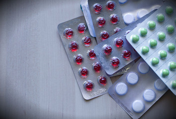 Multi-colored tablets of yellow, red, green color, in foil packaging, lie in the right corner, on a light wooden surface. Medicine, healthcare, protection, treatment for all diseases, overdose. 