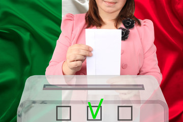 female voter lowers the ballot in a transparent ballot box on the background of the national flag of italy, concept of state election, referendum