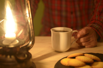 ランタンの灯りでコーヒーを飲む男性