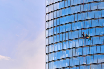 Mens workers in red and dark work clothes cleaning the exterior windows of a business skyscraper -...