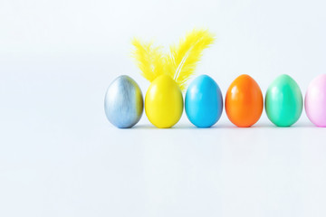 Top view of an easter composition of painted eggs in bright juicy colors on a white background with feather rabbit ears. Vacation concept, flat design, minimalism.