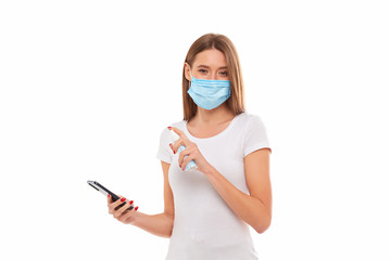Young woman in medical mask washes her mobile phone with a gel antiseptic spray. Conceptual photo on the theme of the epidemic.