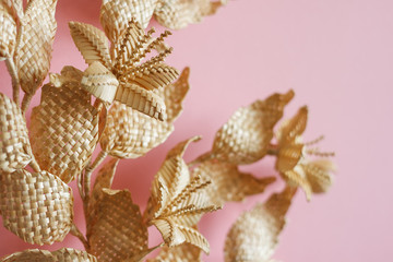 Branch with leaves and flowers is made of straw. Decoration of straw on a pink background. Decor. Fragment closeup. Shallow depth of field (DOF)
