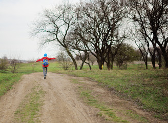a small child a boy in a red jacket and a blue cap is joyfully and happily jumping and jumping on the road in the Park or in the forest. The concept of childhood, spring.