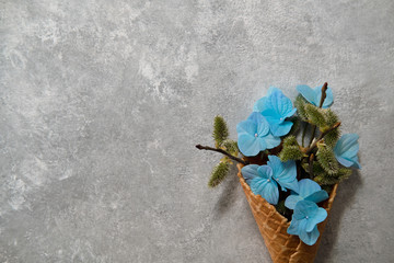 blue hydrangeas and willow twigs in a waffle cone on a gray background.