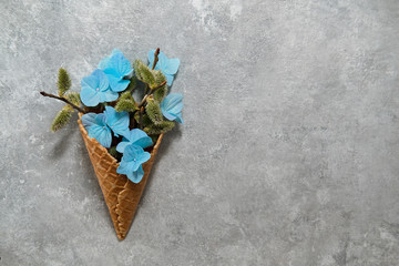 Small  blue flowers and willow twigs in a waffle cone on a gray background. top view
