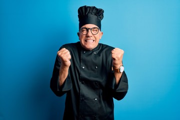 Middle age handsome grey-haired chef man wearing cooker uniform and hat excited for success with arms raised and eyes closed celebrating victory smiling. Winner concept.