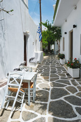 Picturesque narrow street with traditional whitewashed houses with greek flag and cafe tables in Naousa town in famous tourist attraction Paros island, Greece