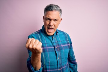 Fototapeta premium Middle age handsome grey-haired man wearing casual shirt over isolated pink background angry and mad raising fist frustrated and furious while shouting with anger. Rage and aggressive concept.