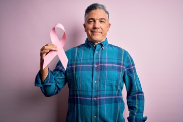 Middle age handsome grey-haired man holding pink cancer ribbon over isolated background with a...