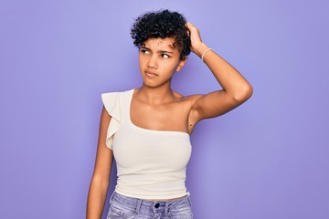 Young beautiful african american afro woman wearing casual t-shirt over purple background confuse...