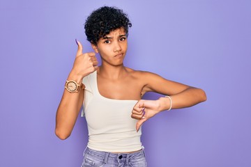 Fototapeta na wymiar Young beautiful african american afro woman wearing casual t-shirt over purple background Doing thumbs up and down, disagreement and agreement expression. Crazy conflict