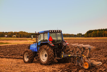 A tractor on a agricultural farming landscape, field with ploving attachment on it