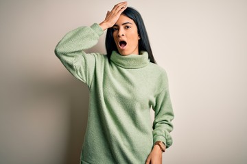 Young beautiful hispanic woman wearing green winter sweater over isolated background surprised with hand on head for mistake, remember error. Forgot, bad memory concept.