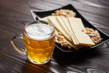 Mug of unfiltered light wheat beer with beer snacks on wooden table