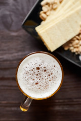 Mug of unfiltered light wheat beer with beer snacks on brown wooden table, top view