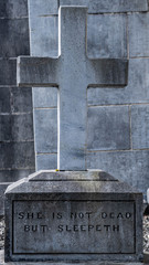 Old cemetery headstone in a graveyard with the words "She is not dead but sleepeth" inscribed on it.