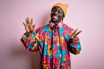 Obraz premium Young handsome african american man wearing colorful coat and cap over pink background showing and pointing up with fingers number seven while smiling confident and happy.