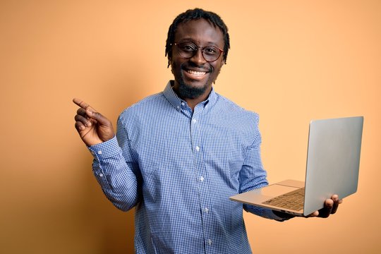 Young african american worker man working using laptop standing over yellow background very happy pointing with hand and finger to the side