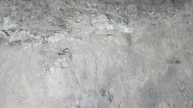 aerial static view of excavators mucking out broken rocks from the quarry mountain