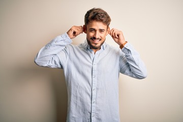 Young handsome man with beard wearing striped shirt standing over white background Smiling pulling ears with fingers, funny gesture. Audition problem