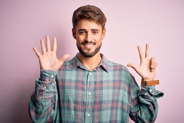 Young handsome man with beard wearing casual shirt standing over pink background showing and pointing up with fingers number eight while smiling confident and happy.