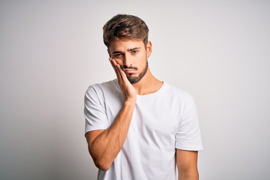 Young handsome man with beard wearing casual t-shirt standing over white background thinking looking tired and bored with depression problems with crossed arms.