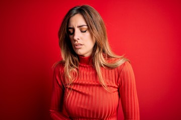 Young beautiful brunette woman wearing casual turtleneck sweater over red background with hand on stomach because indigestion, painful illness feeling unwell. Ache concept.