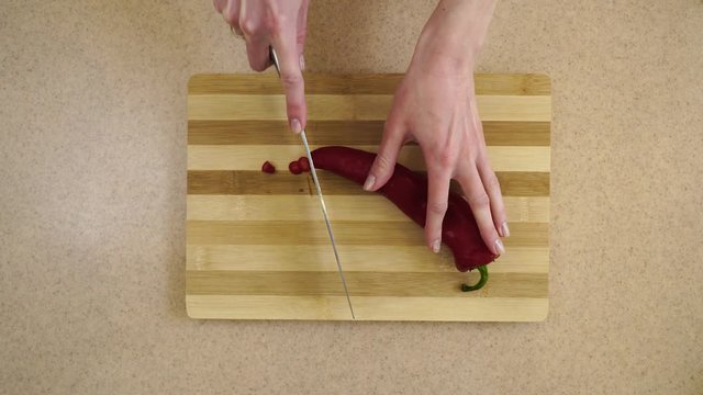 Medium shot. Woman&rsquo;s hands are cutting sweet red pepper Kapi on the rings on a kitchen board by a metal knife. (a view from the top)