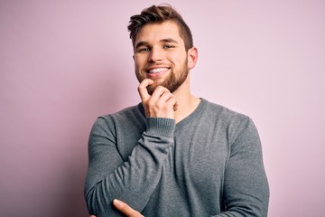 Young handsome blond man with beard and blue eyes wearing casual sweater looking confident at the camera with smile with crossed arms and hand raised on chin. Thinking positive.