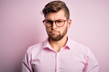 Obraz premium Young handsome blond man with beard and blue eyes wearing pink shirt and glasses depressed and worry for distress, crying angry and afraid. Sad expression.